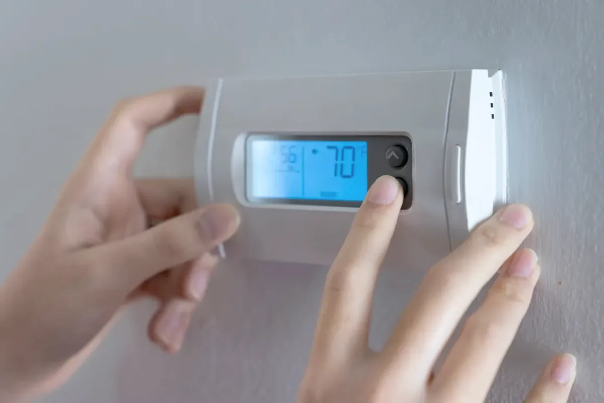 Hands adjusting a digital wall thermostat